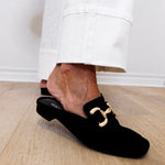 Black loafers with gold buckles worn by a person on a wooden floor.