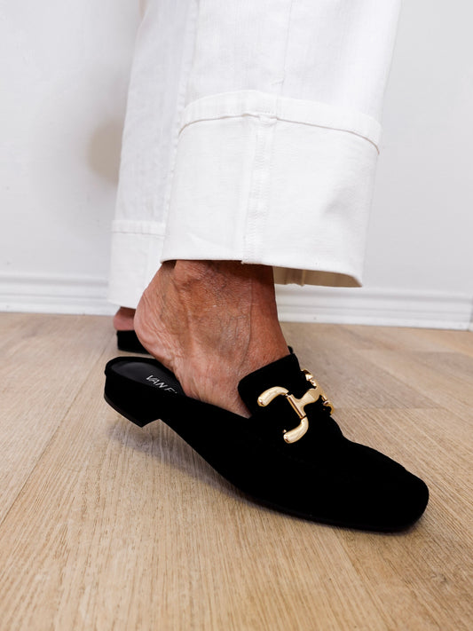 Black loafers with gold buckles worn by a person on a wooden floor.
