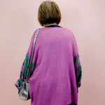 Person wearing a purple cardigan with floral sleeves against a pink background