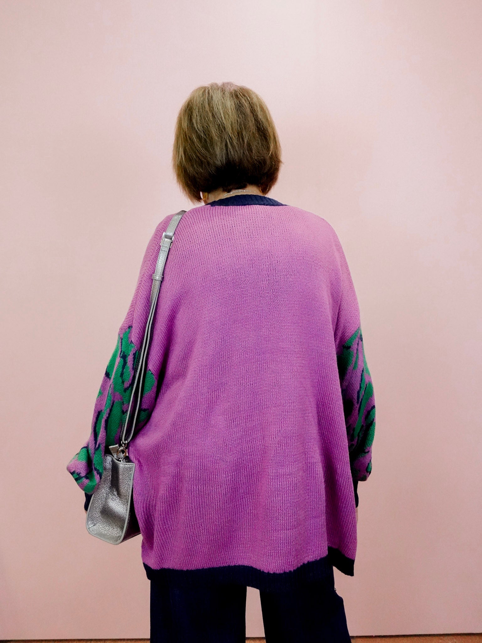 Person wearing a purple cardigan with floral sleeves against a pink background