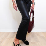 Person wearing black leather pants and black loafers with a white wall background