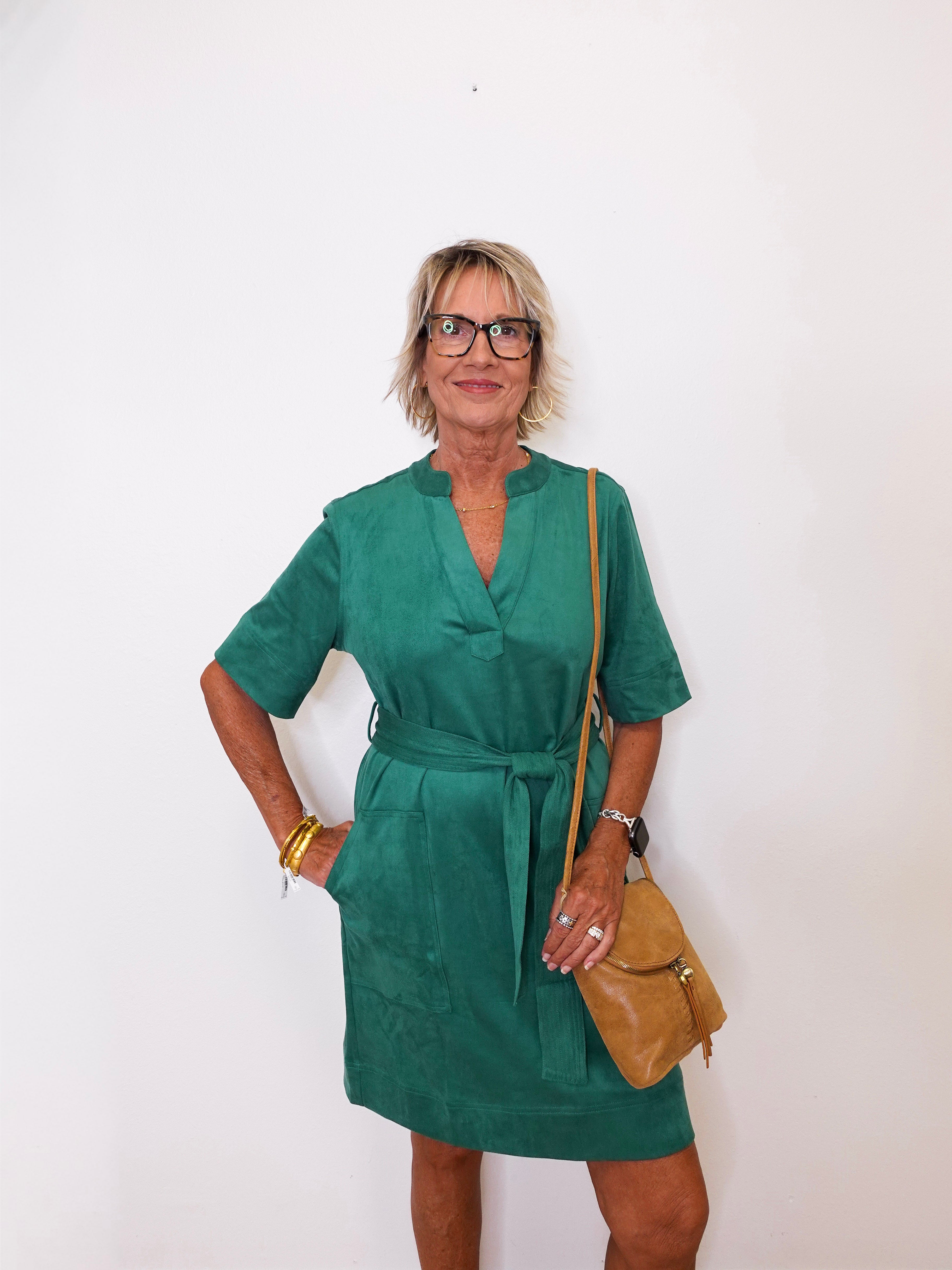 Woman wearing a green dress with a brown bag against a white background