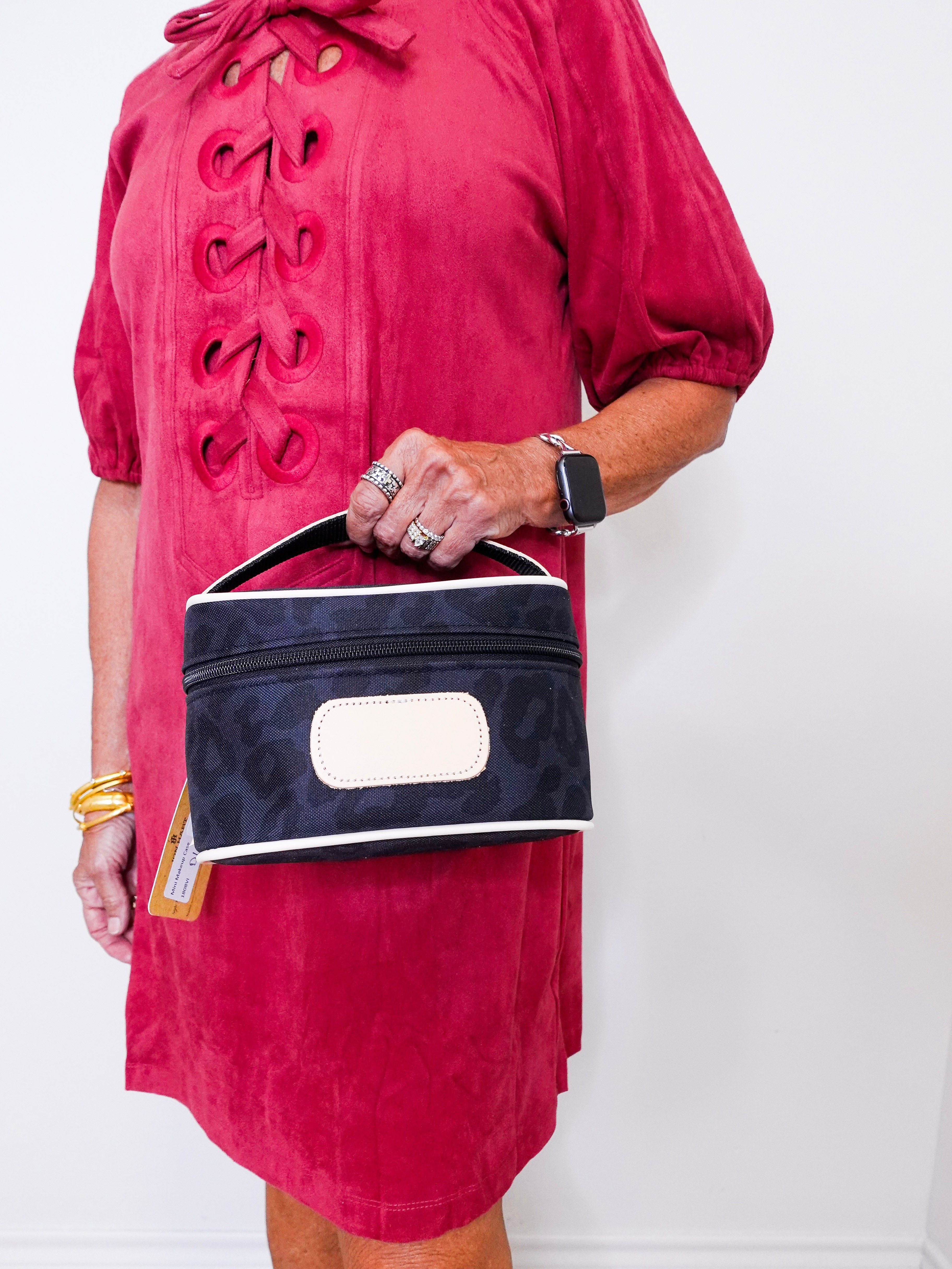 Person wearing a red dress holding a navy blue handbag with a white label against a white background