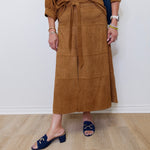 Person wearing a brown skirt with a white wall background