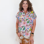 Woman wearing a colorful patterned shirt holding a brown handbag against a white background