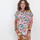 Woman wearing a colorful patterned shirt holding a brown handbag against a white background