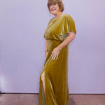 Model wearing a gold velvet maxi dress with flutter sleeves and side slit, styled with gold jewelry for an elegant, polished look.
