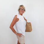 Woman wearing a white blouse and beige shorts, holding a brown bag against a white background