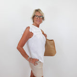 Woman wearing a white blouse and beige shorts, holding a brown bag against a white background