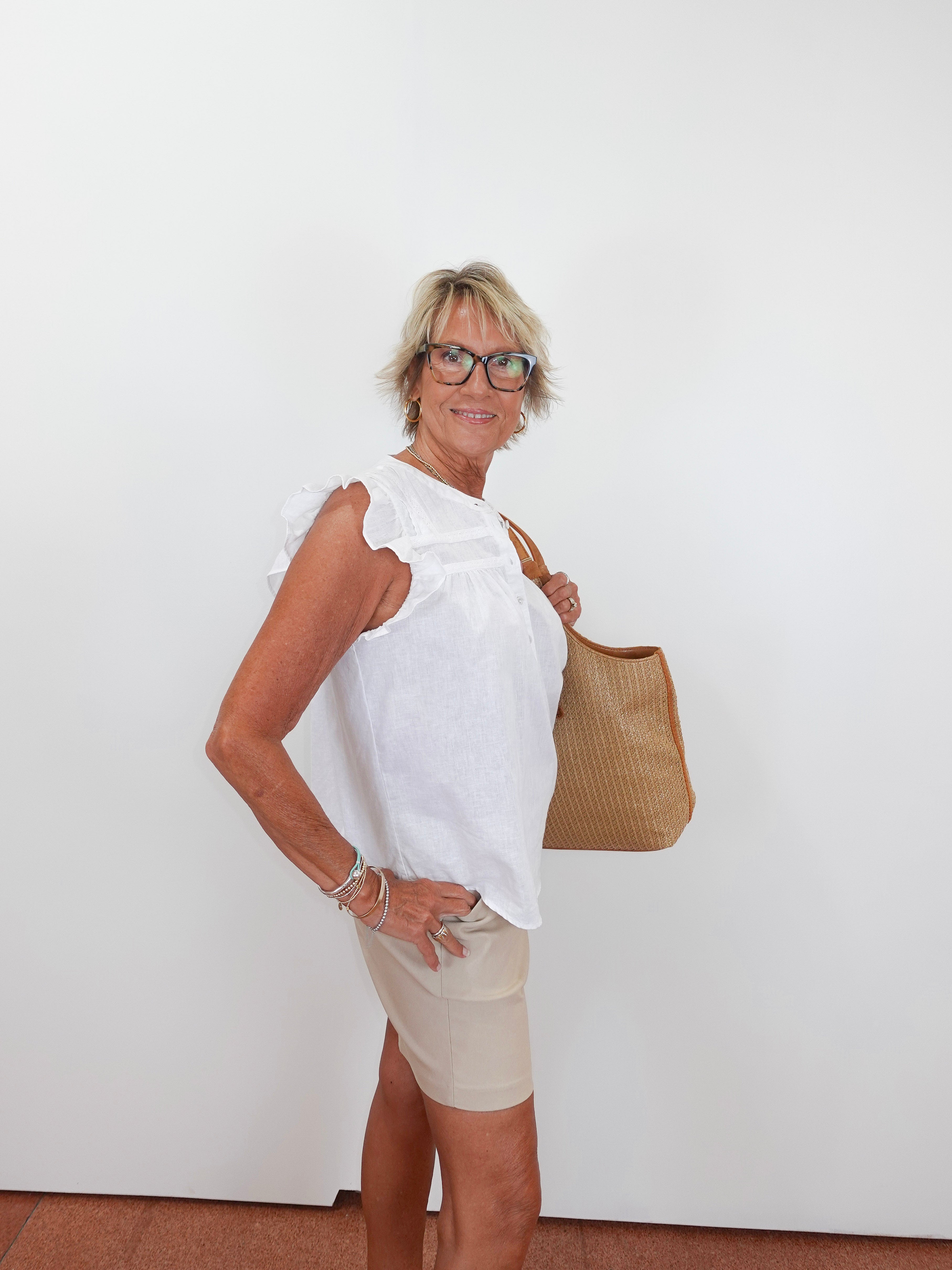 Woman wearing a white blouse and beige shorts, holding a brown bag against a white background