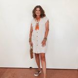 Woman wearing a white dress with an orange scarf against a plain background