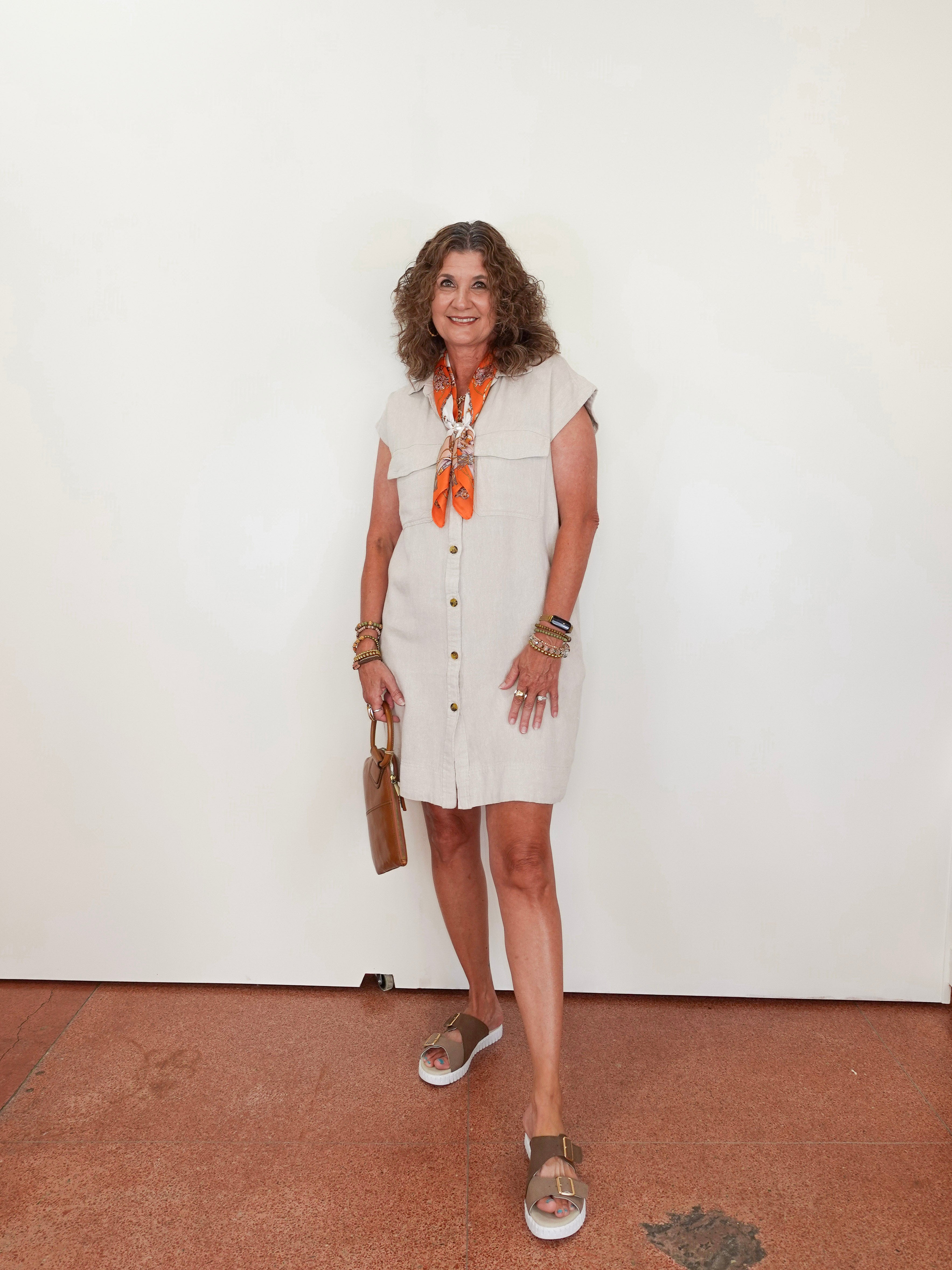 Woman wearing a white dress with an orange scarf against a plain background