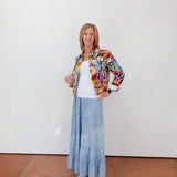 Woman wearing a floral jacket, white top, and blue skirt against a white wall.