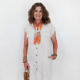 Woman wearing a white dress with an orange scarf, holding a brown bag against a white background
