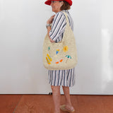 Woman wearing a red hat and striped outfit with a woven bag against a white wall.