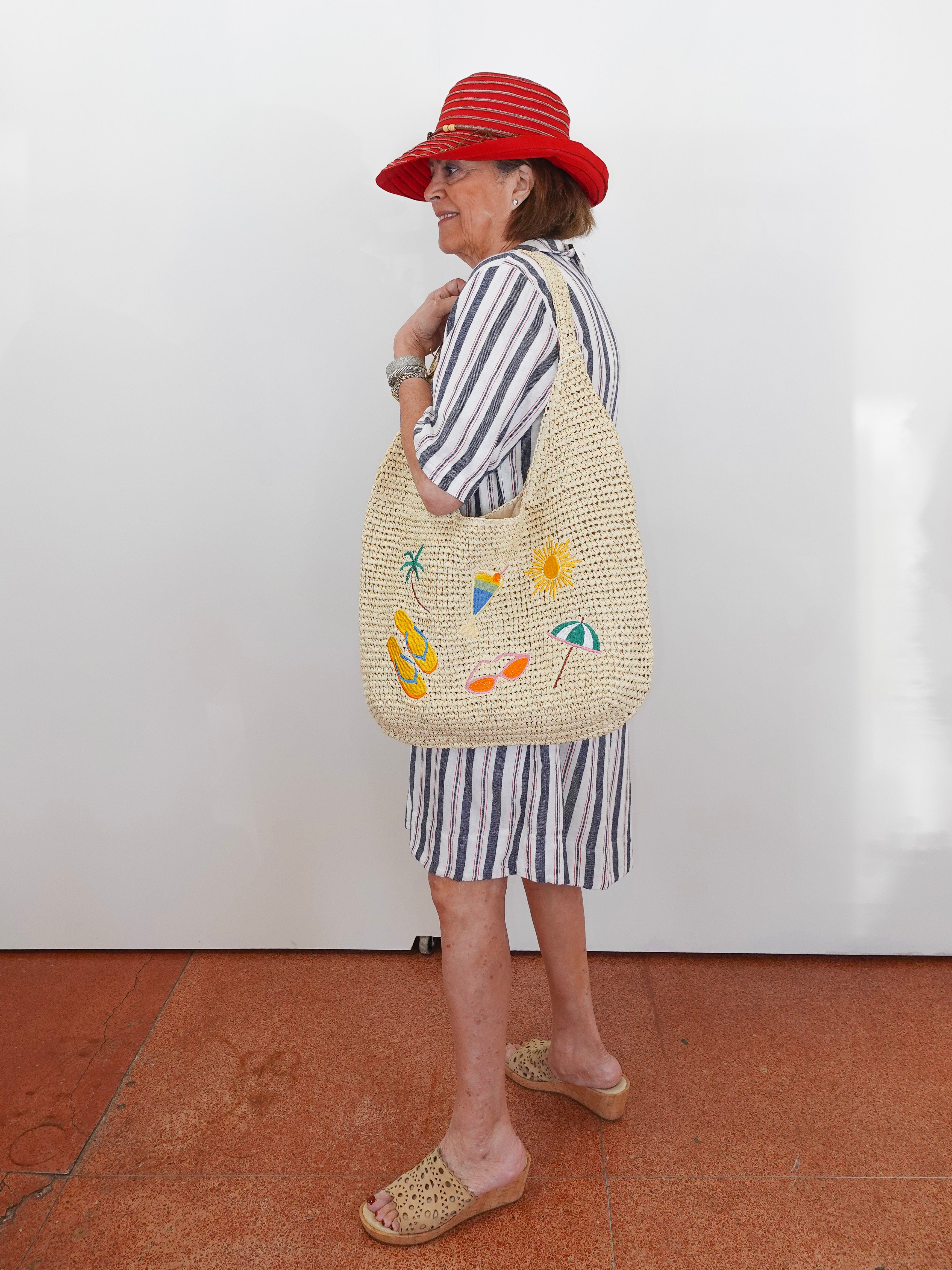 Woman wearing a red hat and striped outfit with a woven bag against a white wall.