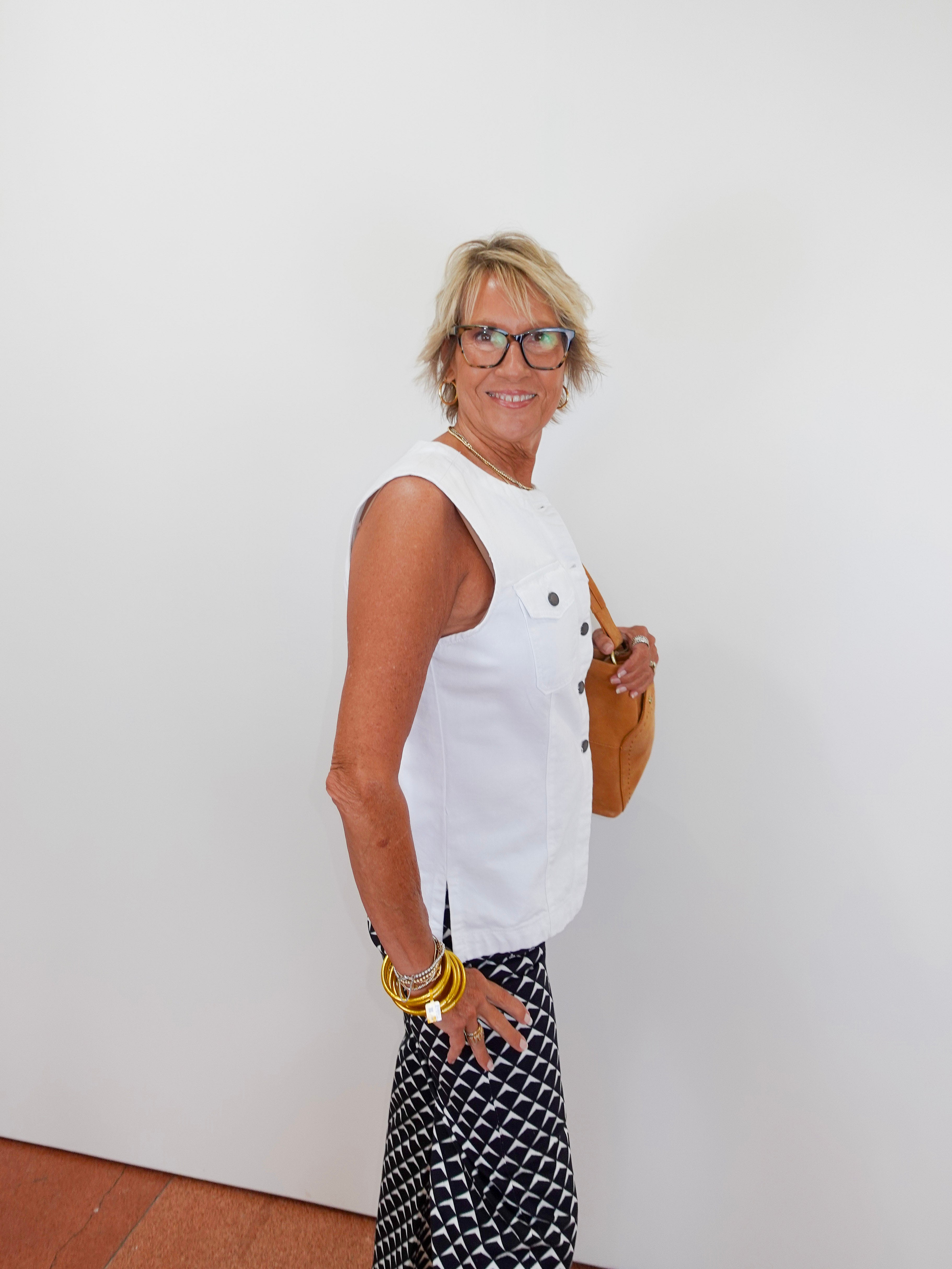 Woman wearing a white sleeveless top and patterned skirt against a plain background
