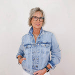 Person wearing a denim jacket and white pants against a plain background