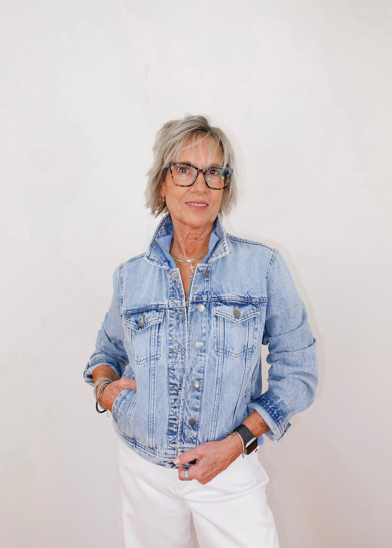 Person wearing a denim jacket and white pants against a plain background