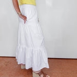 Person wearing a white ruffled skirt and yellow top against a plain background