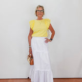 Woman wearing a yellow top and white skirt against a plain background