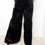 Person wearing black velvet wide-leg pants against a white background