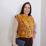 Woman wearing a patterned yellow vest against a white wall