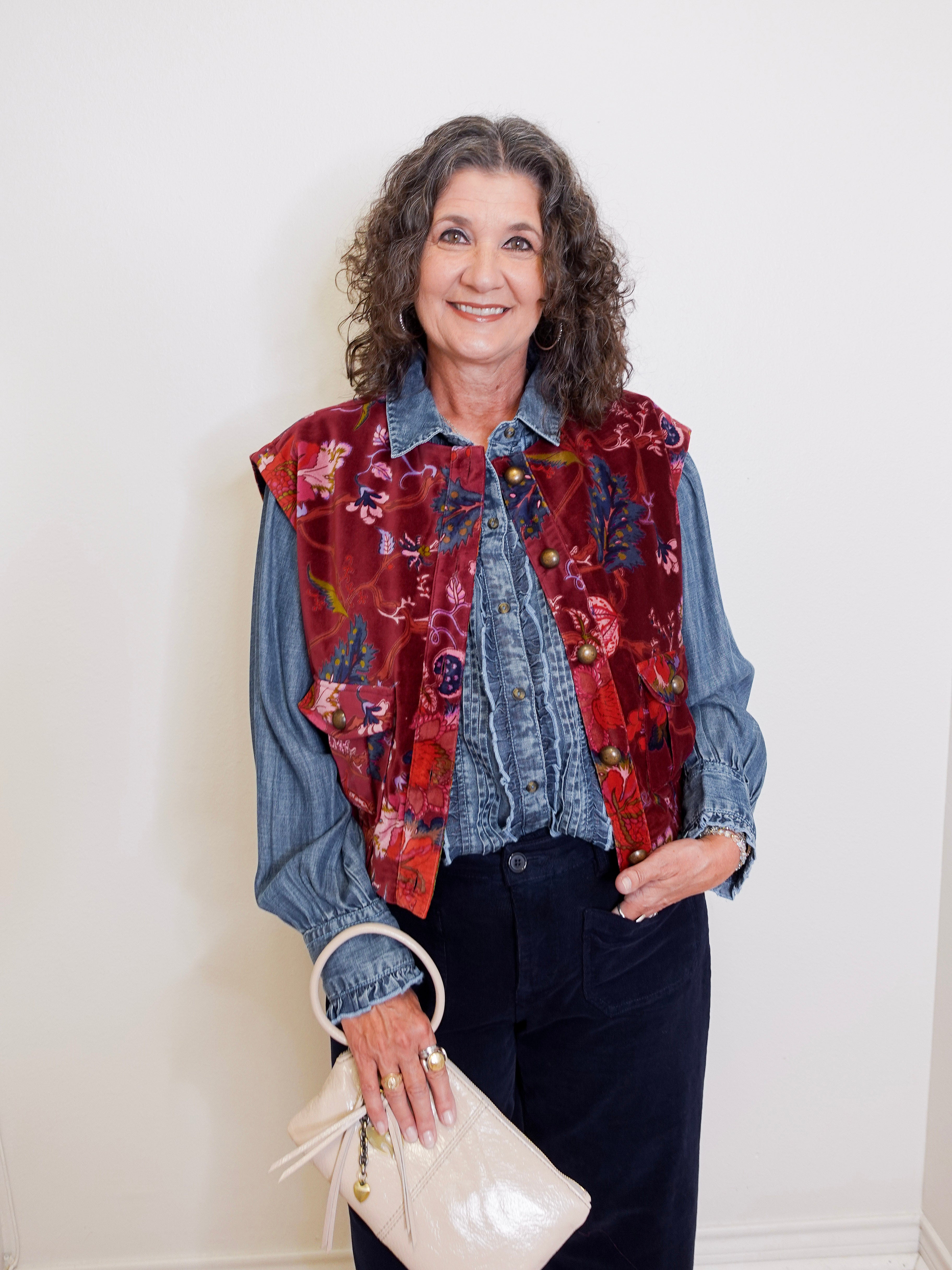 Woman wearing a colorful vest over a denim shirt with a white background