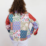 Person wearing a colorful patchwork blouse with long sleeves against a white wall.