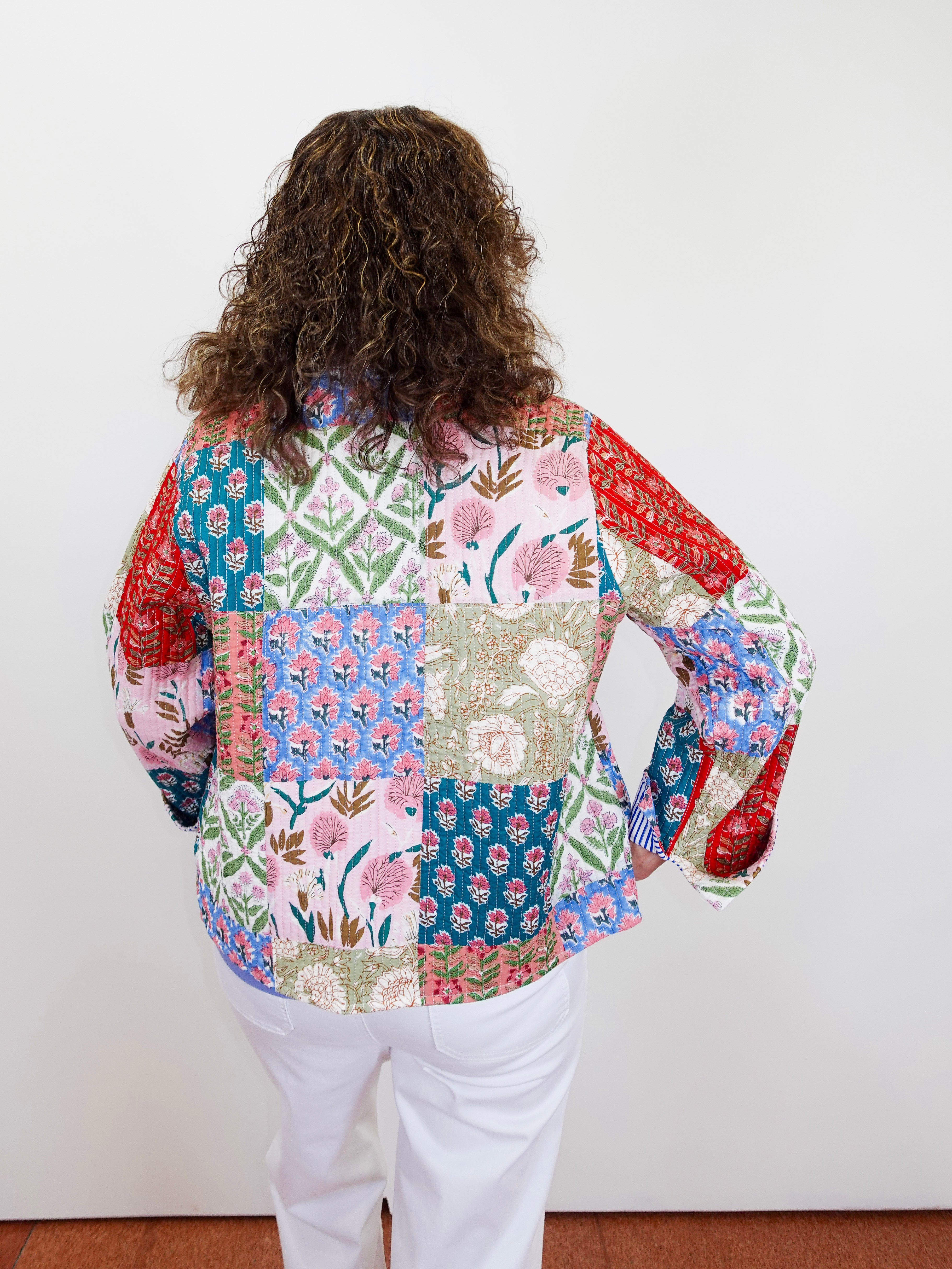 Person wearing a colorful patchwork blouse with long sleeves against a white wall.