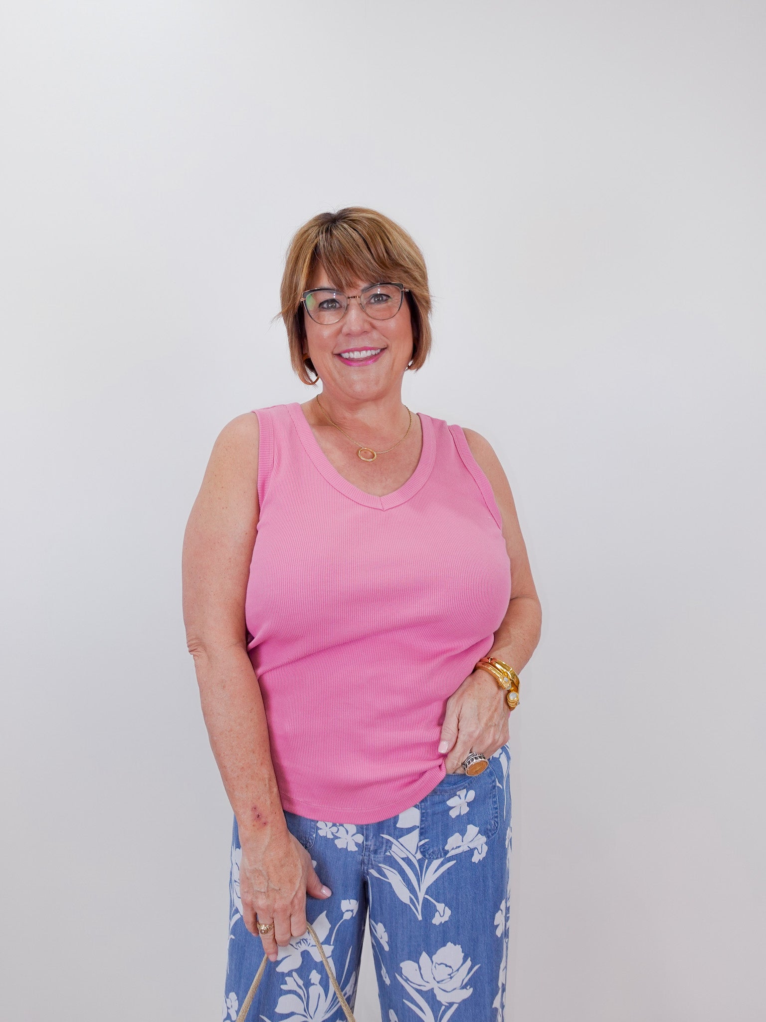 Woman wearing a pink tank top and blue floral pants against a white background