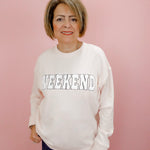 Woman wearing a white sweatshirt with 'Weekend' text on a pink background