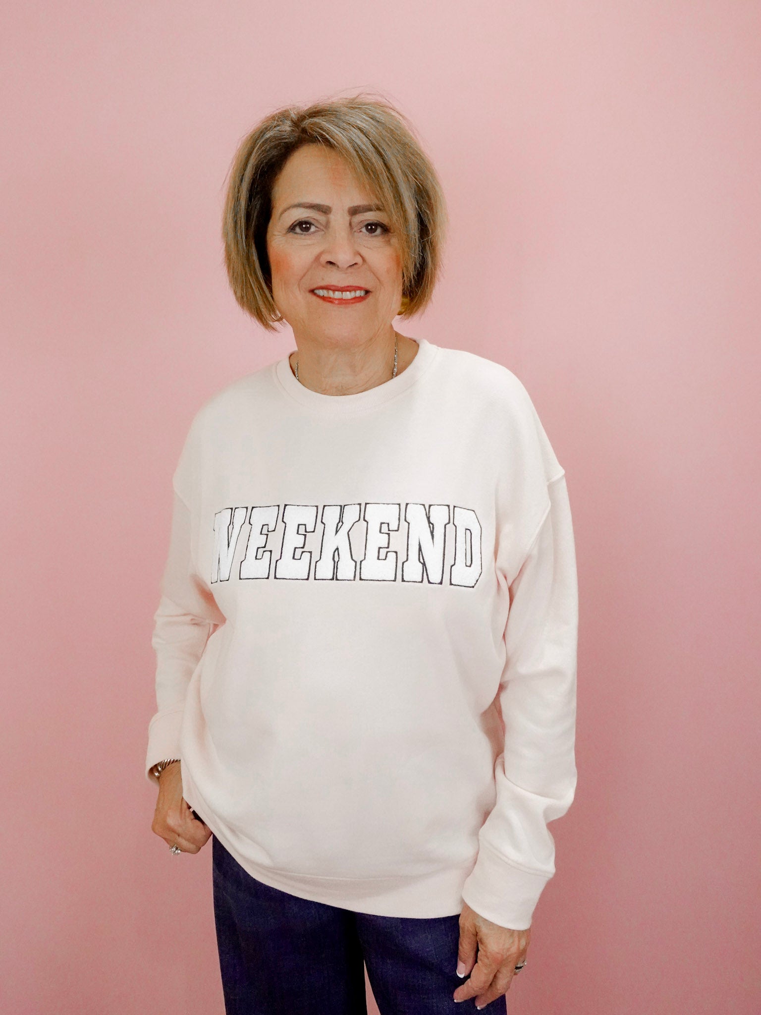 Woman wearing a white sweatshirt with 'Weekend' text on a pink background