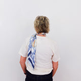 Person wearing a white shirt with a colorful scarf draped over their shoulder against a plain background