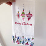 Hand holding a Christmas-themed towel with decorative ornaments and 'Merry Christmas' text.