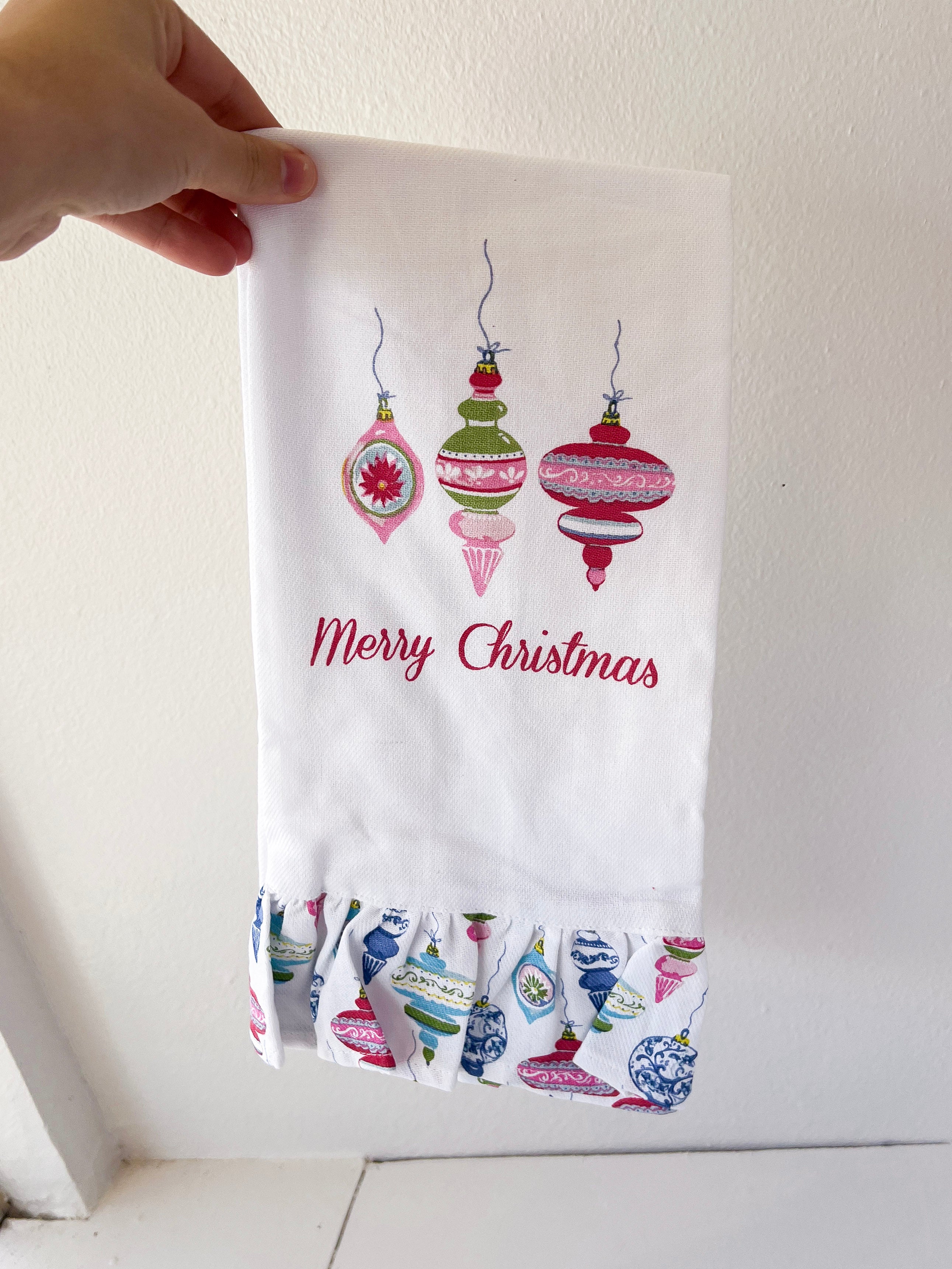 Hand holding a Christmas-themed towel with decorative ornaments and 'Merry Christmas' text.