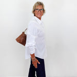 Person wearing a white shirt and dark pants with a brown bag against a white background