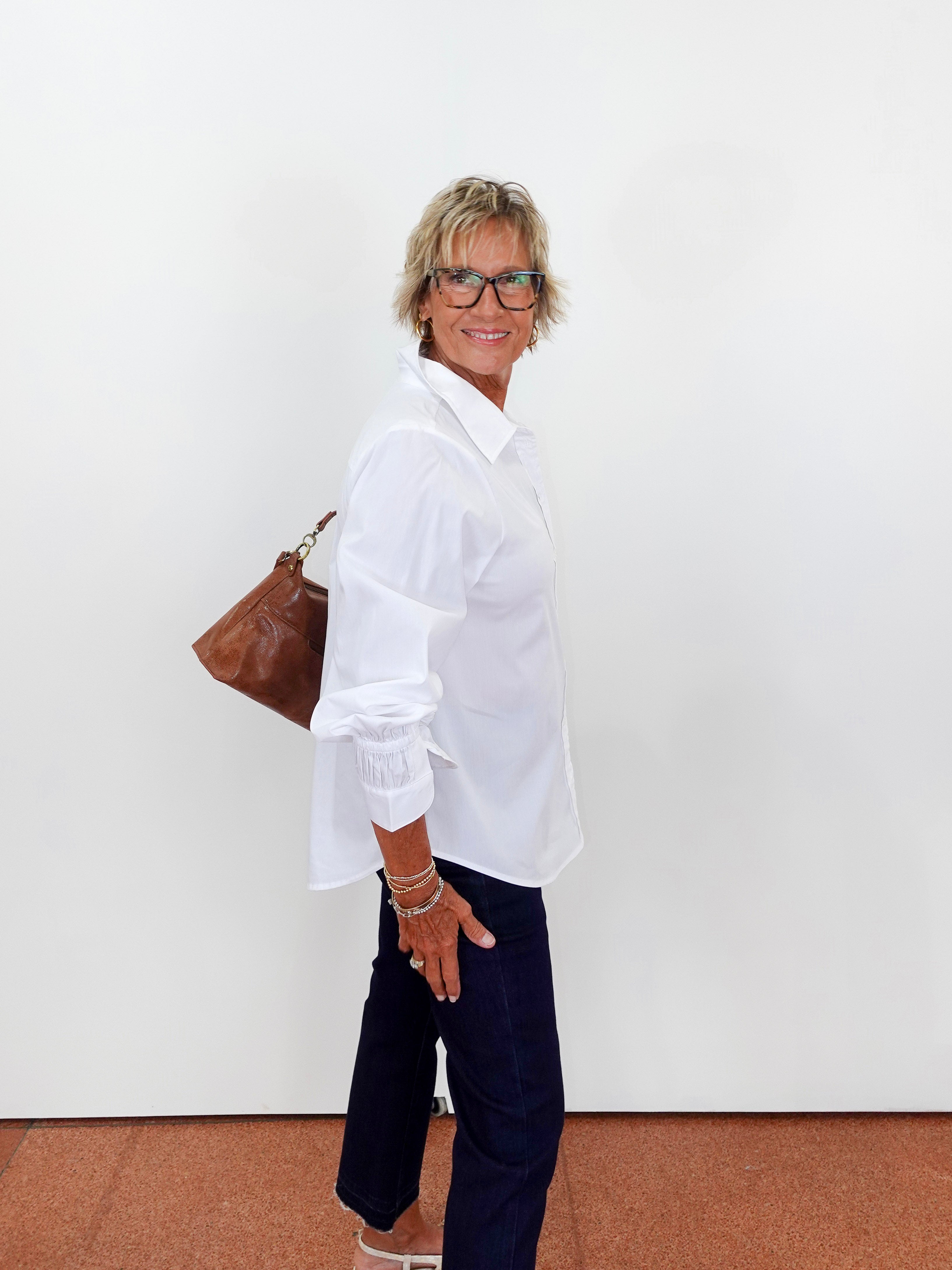 Person wearing a white shirt and dark pants with a brown bag against a white background