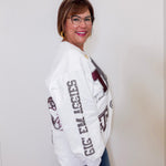 Woman wearing a white sweatshirt with text and graphics, standing against a plain background