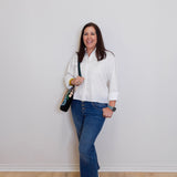 Woman wearing a white shirt, blue jeans, and red shoes against a plain white wall.