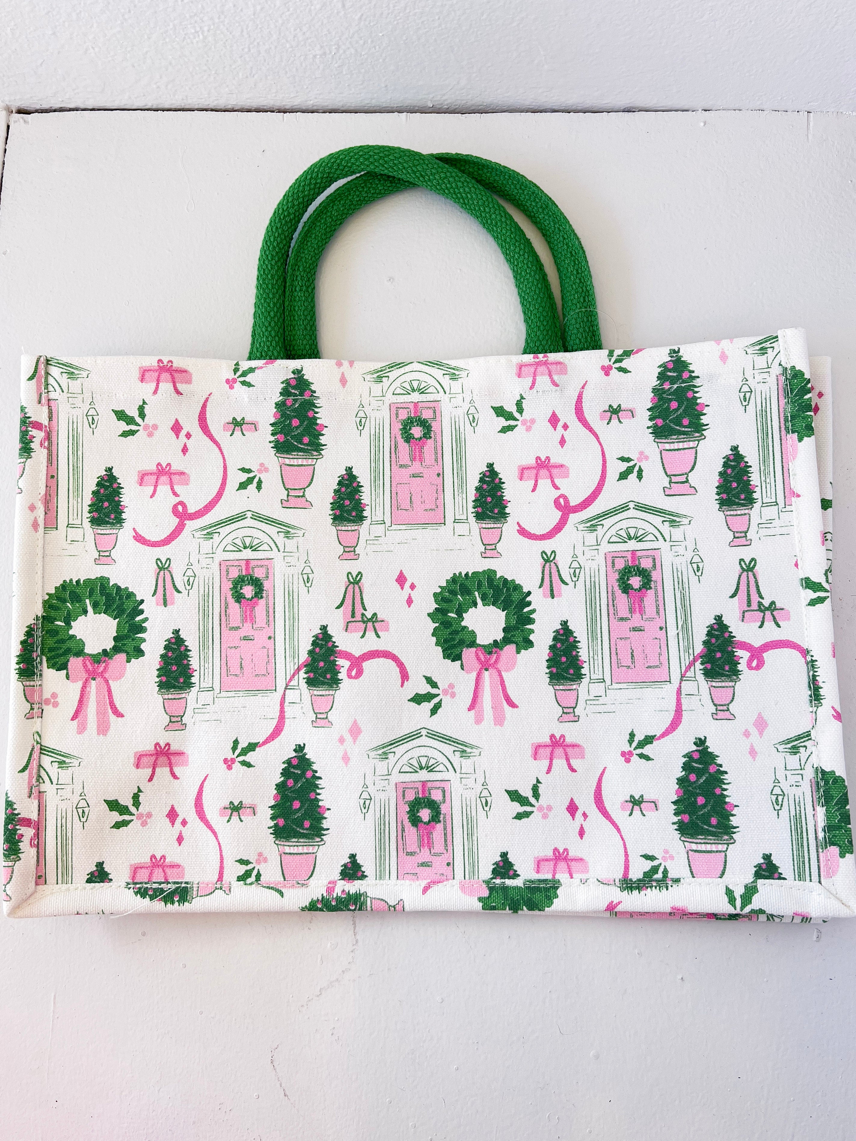 Tote bag with festive design featuring trees, wreaths, and pink ribbons on a white background.