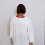 Person wearing a white blouse against a plain background