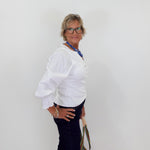Woman wearing a white blouse and dark pants against a plain background