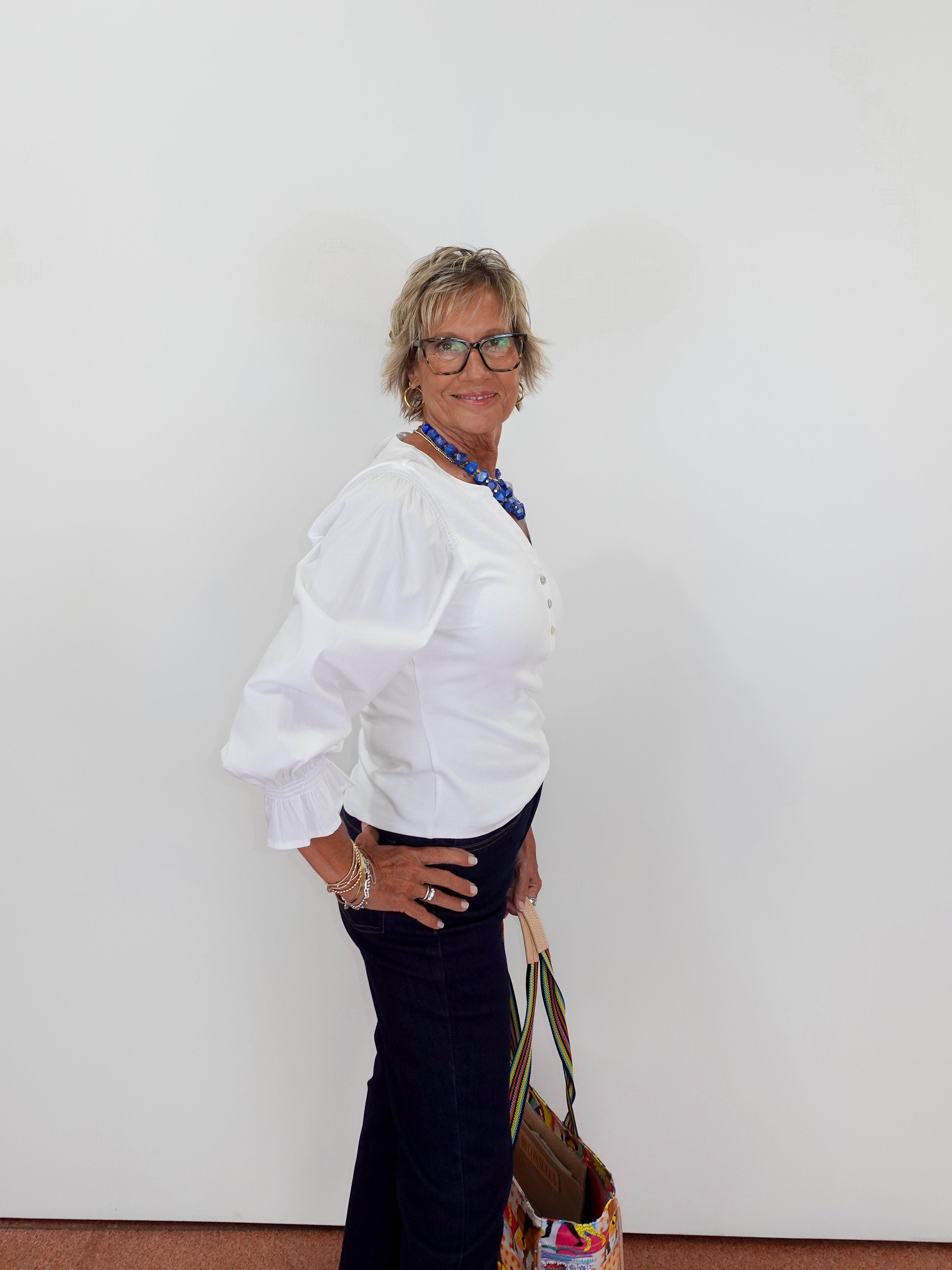 Woman wearing a white blouse and dark pants against a plain background