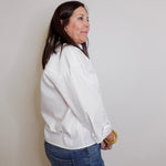 Woman wearing a white jacket and blue jeans against a plain background
