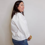 Woman wearing a white jacket and blue jeans against a plain background