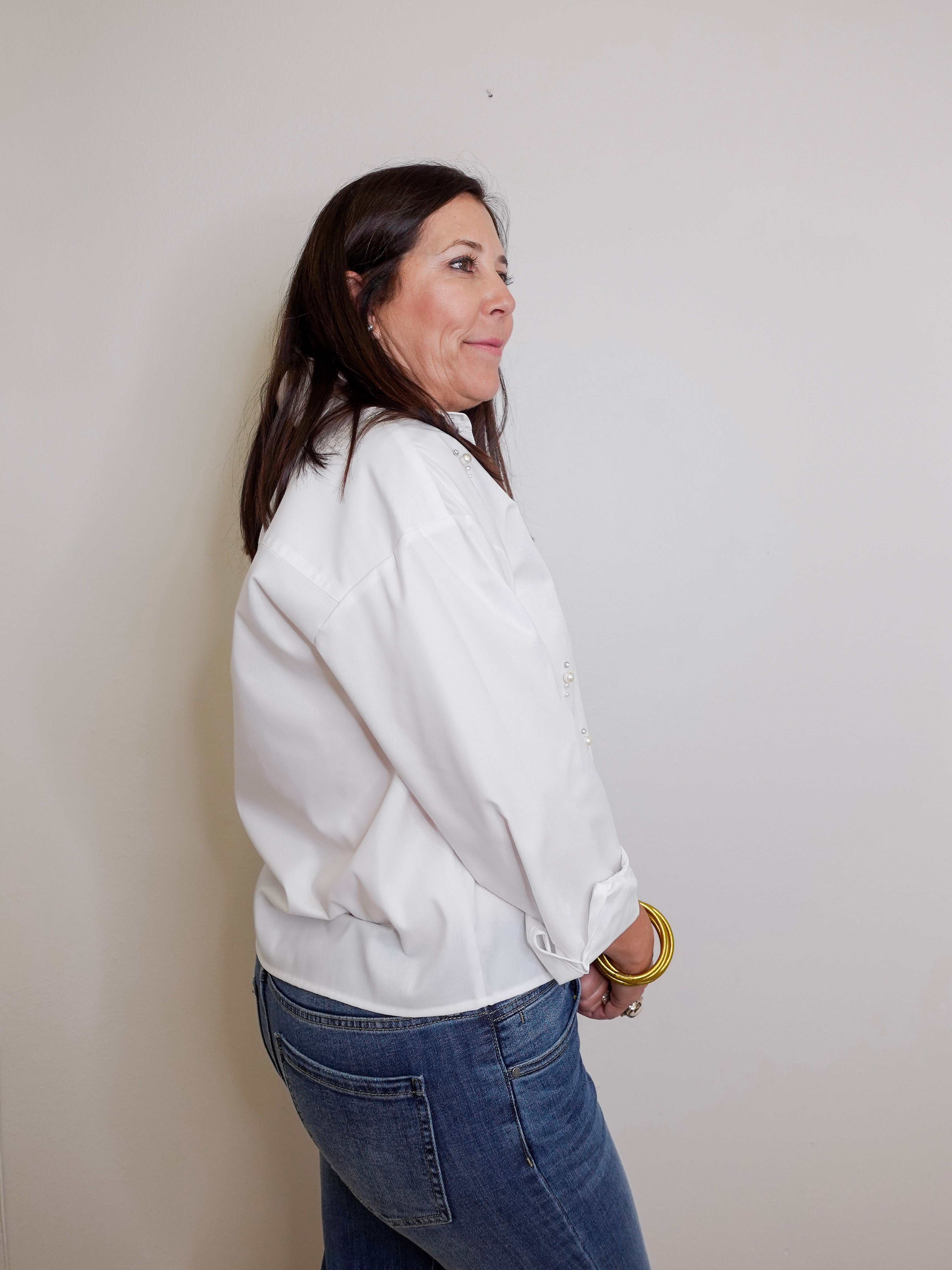 Woman wearing a white jacket and blue jeans against a plain background
