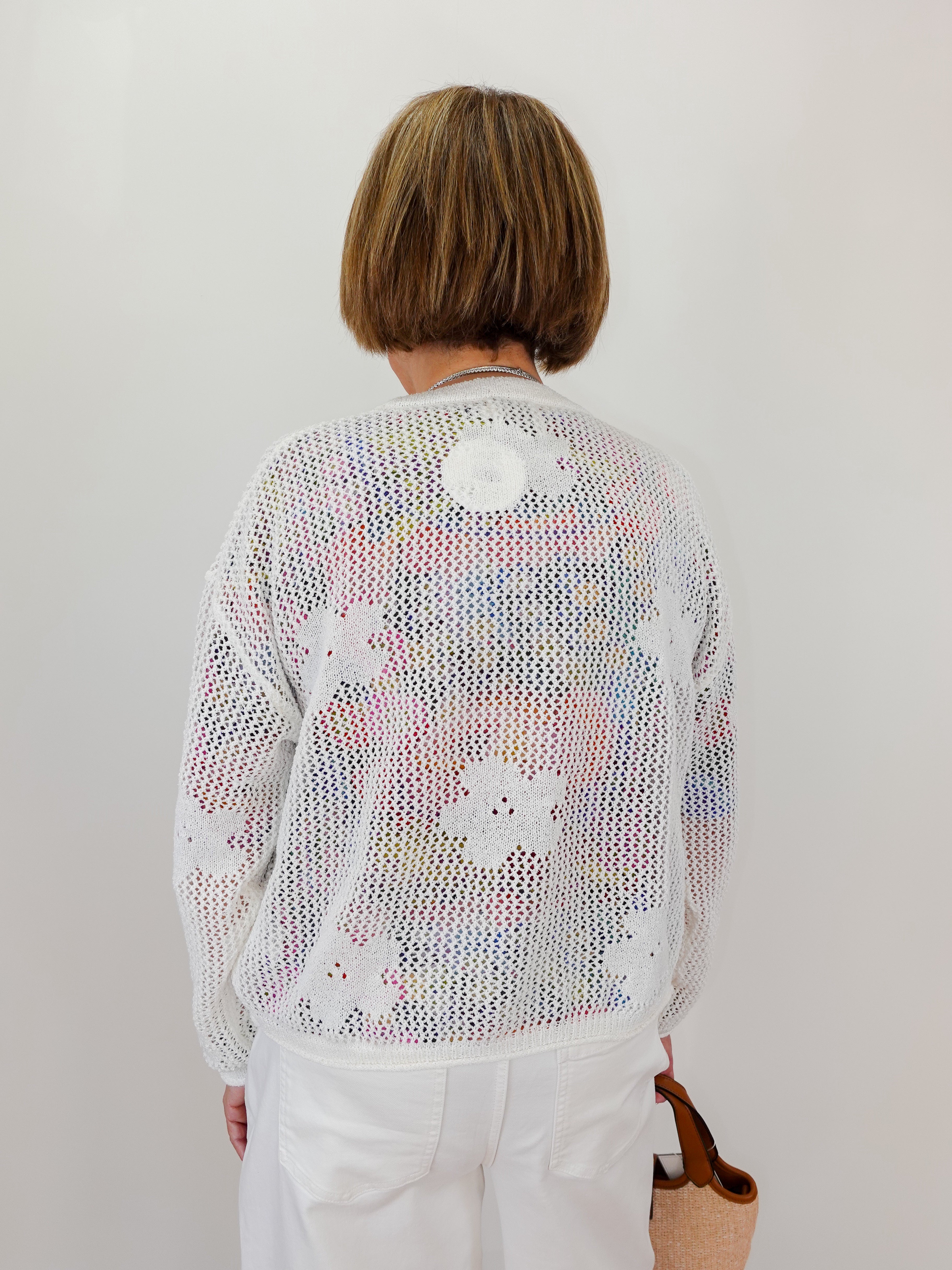Person wearing a light-colored knit cardigan with floral patterns on a plain background