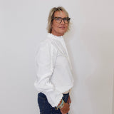 Person wearing a white blouse and blue jeans against a plain background