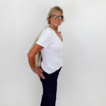 Woman wearing a white t-shirt and dark pants against a plain white wall.